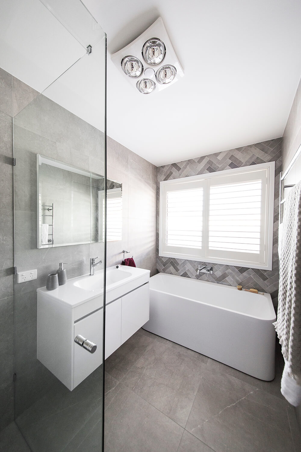 A custom designed bathroom featuring grey tiles and white plantain shutters. Designed and built by MJ Harris Group. #MJHxAbbingtonCres