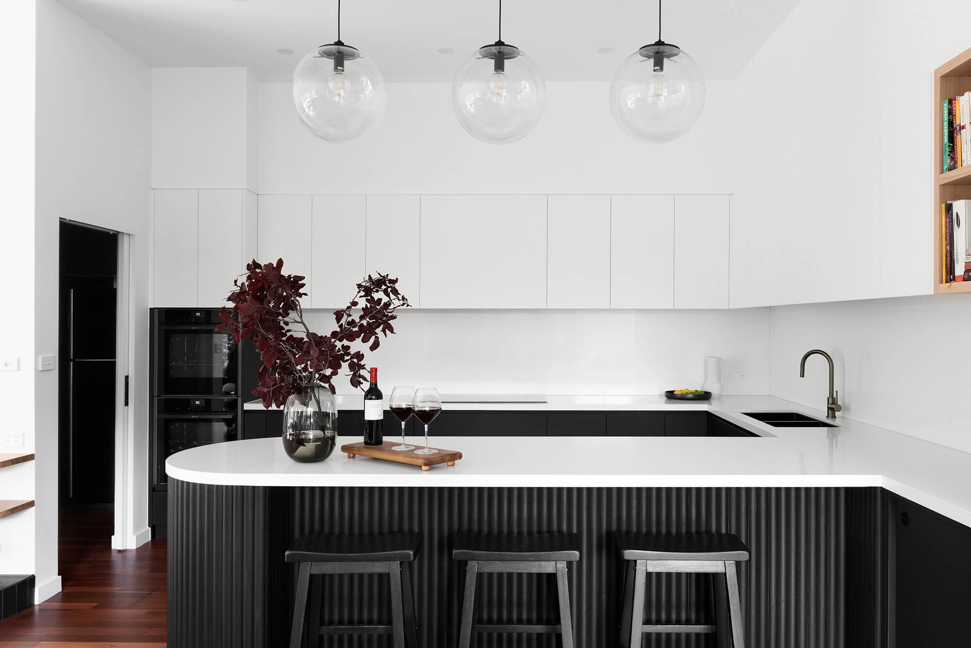 A custom designed kitchen featuring a monochromatic curved island bench. Designed and built by MJ Harris Group.