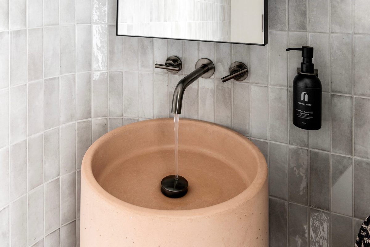 A custom designed bathroom featuring a curved tiled feature wall and pink concrete pillar basin. Designed and built by MJ Harris Group. #MJHxPeppinSt
