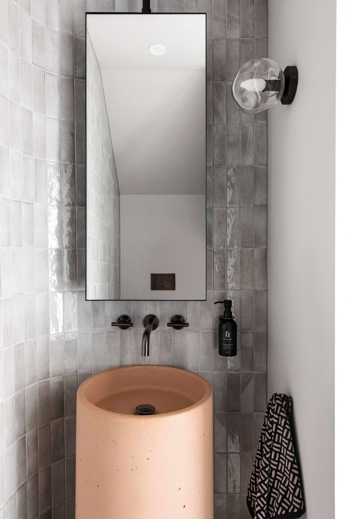 A custom designed bathroom featuring a curved tiled feature wall and pink concrete pillar basin. Designed and built by MJ Harris Group. #MJHxPeppinSt