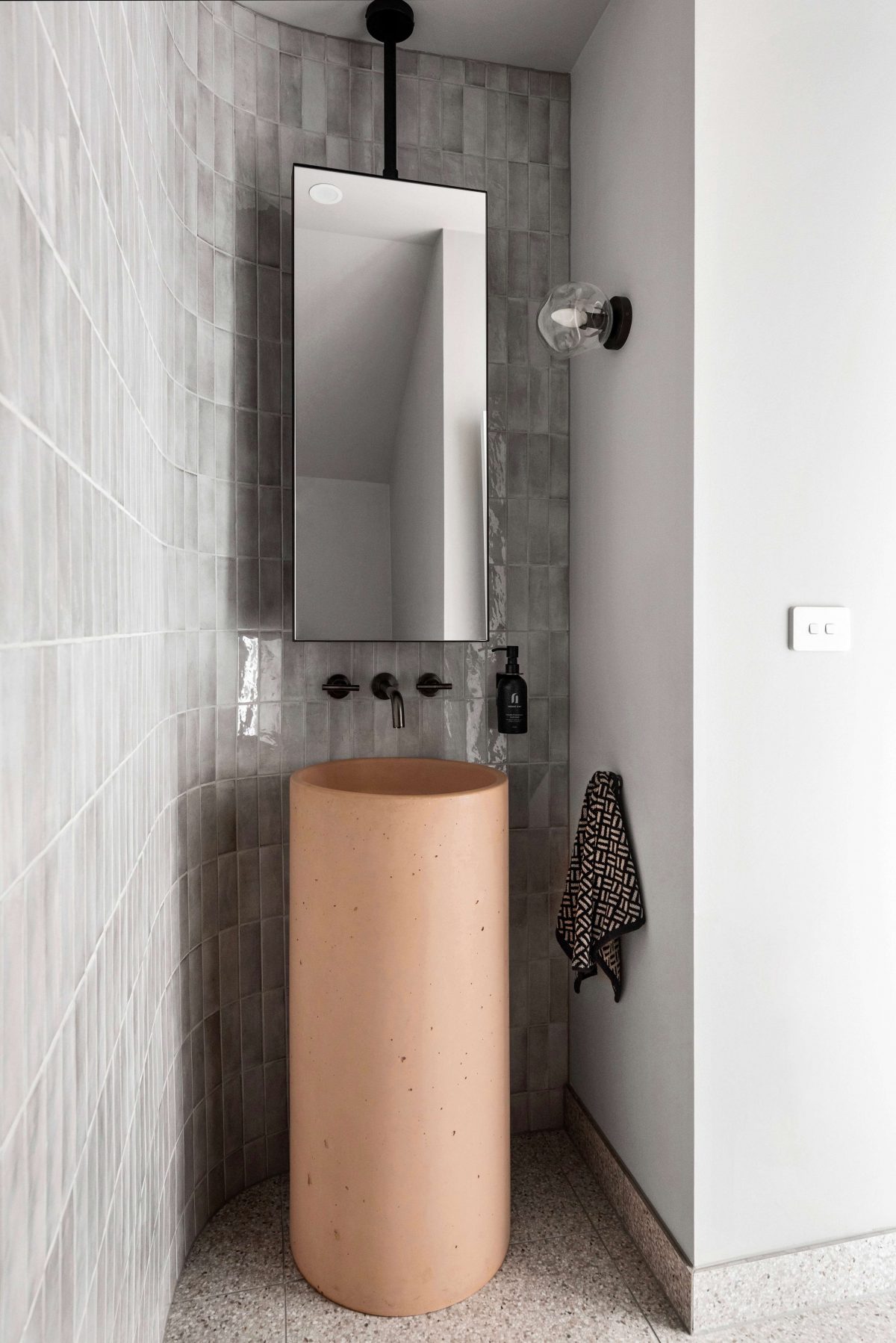 A custom designed bathroom featuring a curved tiled feature wall and pink concrete pillar basin. Designed and built by MJ Harris Group. #MJHxPeppinSt