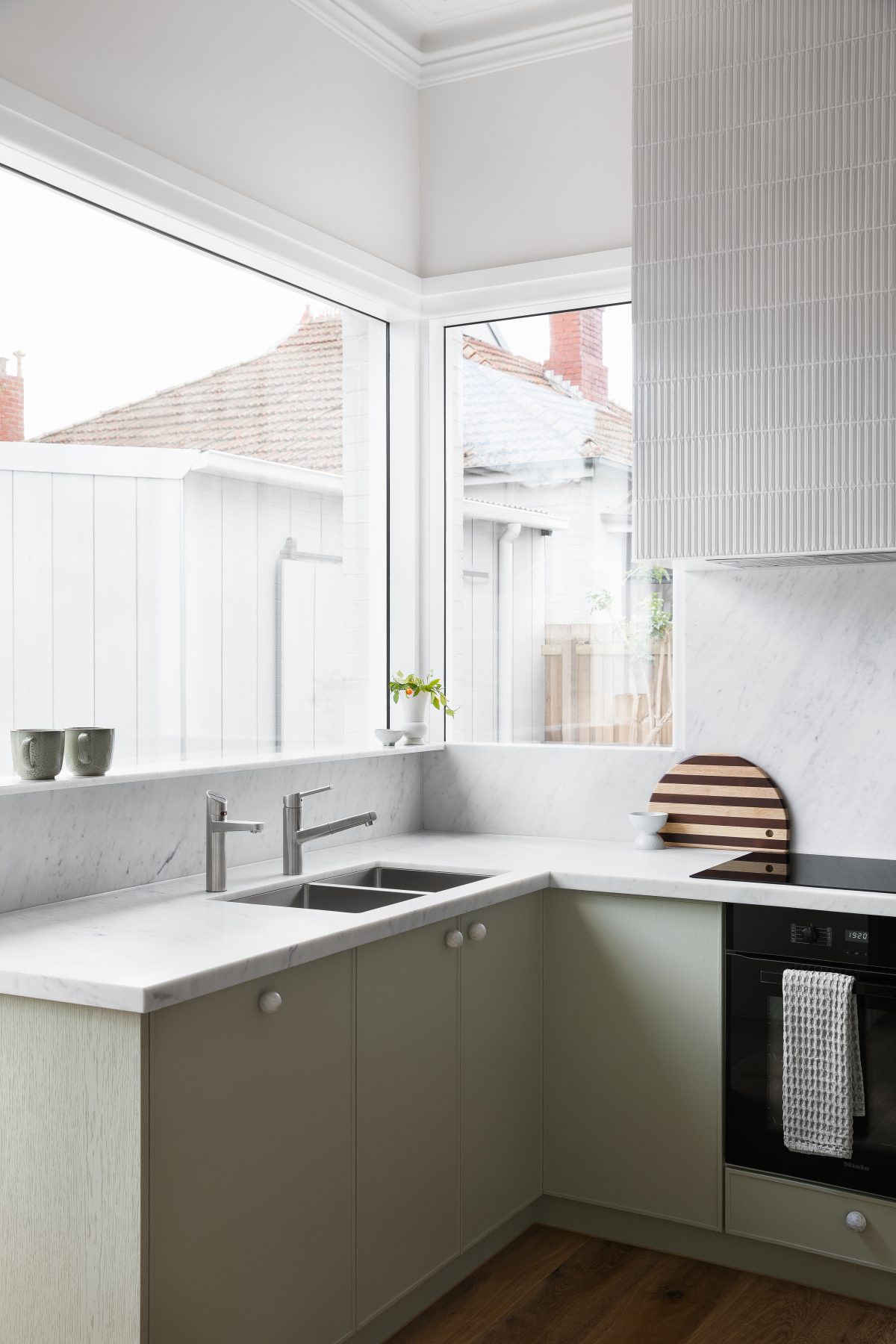 A custom designed kitchen featuring custom joinery in green and a Carrara Marble bench top. Designed and built by MJ Harris Group.