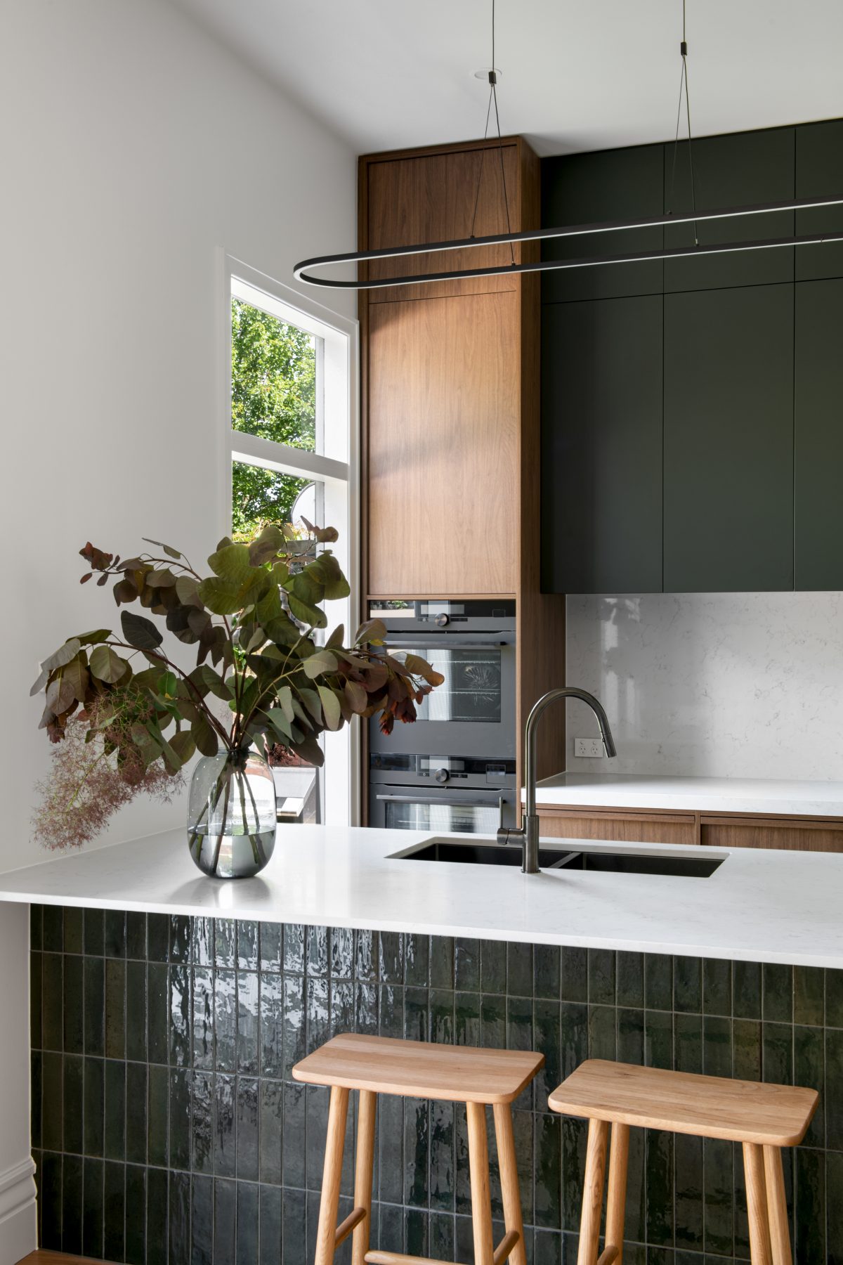 A custom designed kitchen featuring walnut joinery and handmade gloss green tiles. Designed and built by MJ Harris Group.