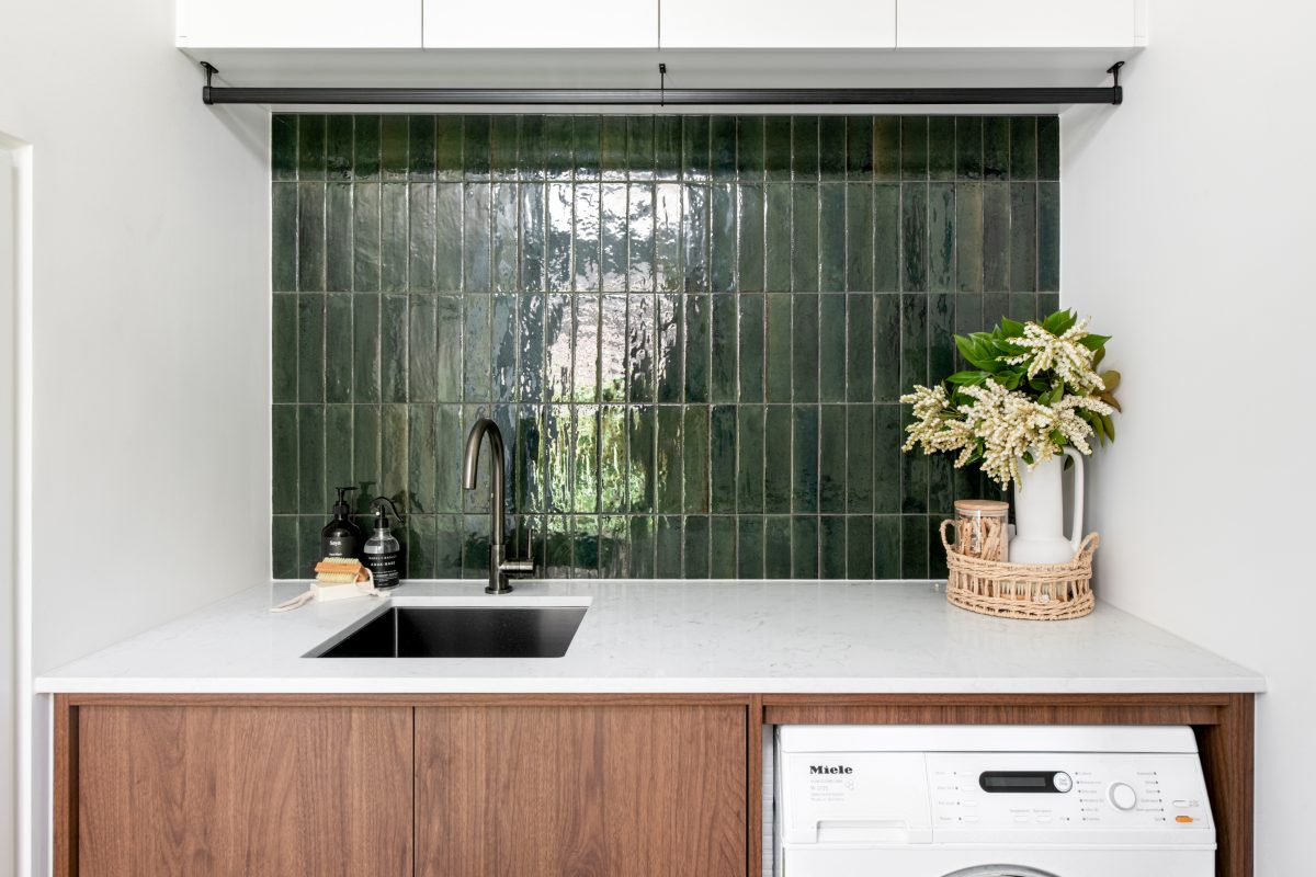 A custom designed laundry featuring walnut joinery and handmade gloss green tiles. Designed and built by MJ Harris Group.